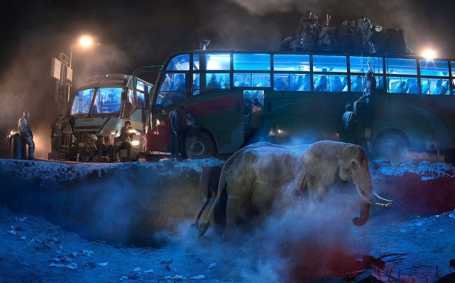 Image of bus station with elephant in the foreground and bus station and people in the background