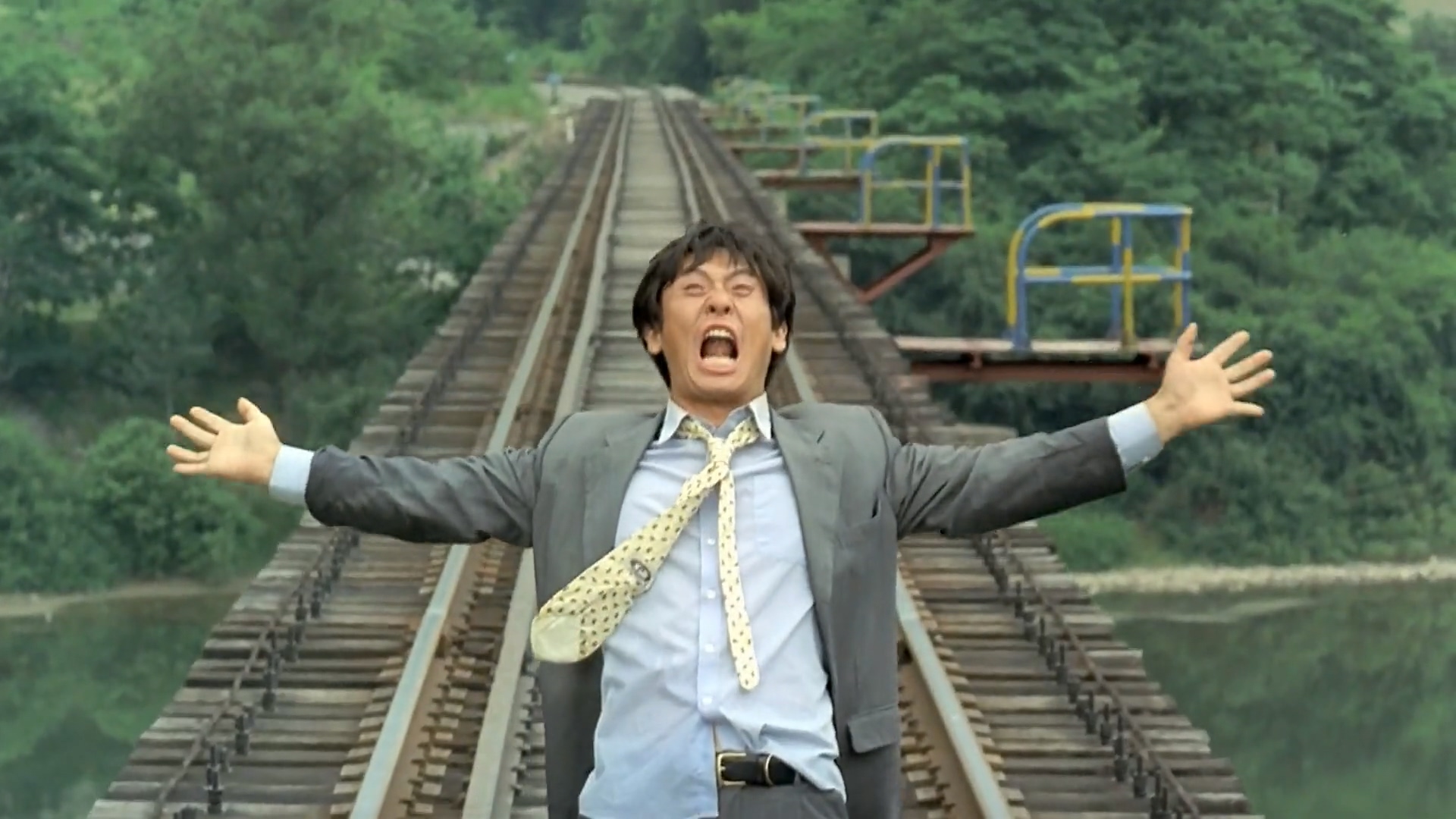Man yelling with arms wide while standing on empty train tracks